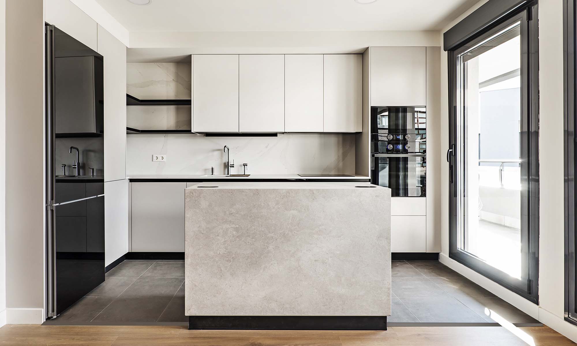 Front view of a modern designer kitchen with smooth handleless cabinets with black edges, black glass appliances, a marble island and marble countertops